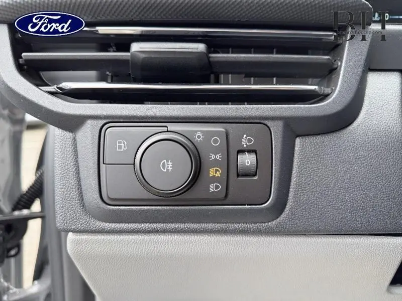 Gros plan sur le tableau de bord gris du Ford Transit Custom, montrant la commande des phares et la ventilation.