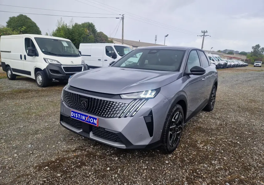 Peugeot 3008 gris Artense vue 3/4 avant droit, avec calandre distinctive et phares LED allumés sur terrain gravillonné.