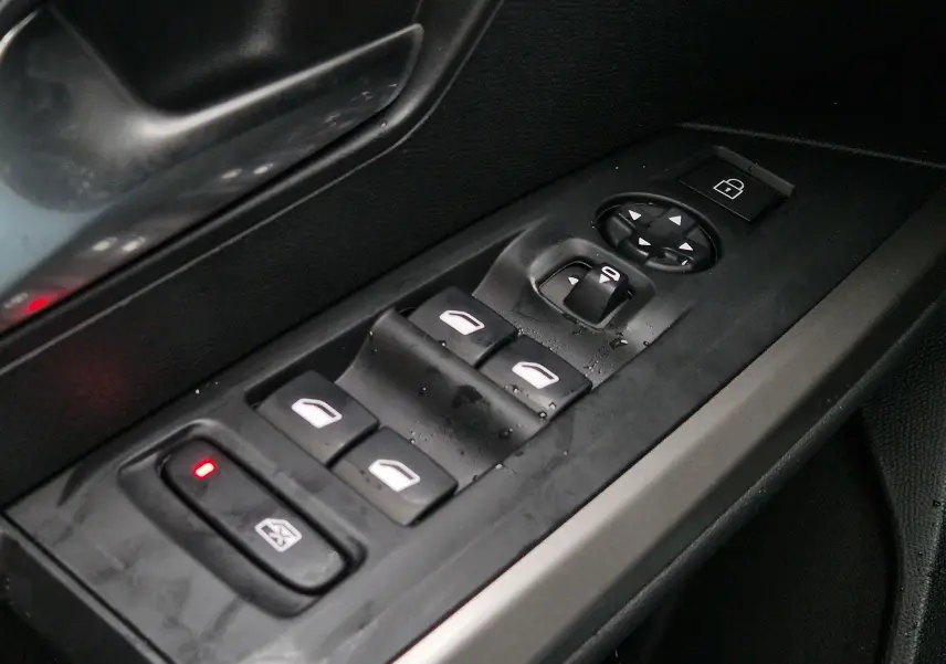 Gros plan sur la commande des vitres et rétroviseurs côté gauche intérieur d’un Peugeot 3008 gris Artense 2025.