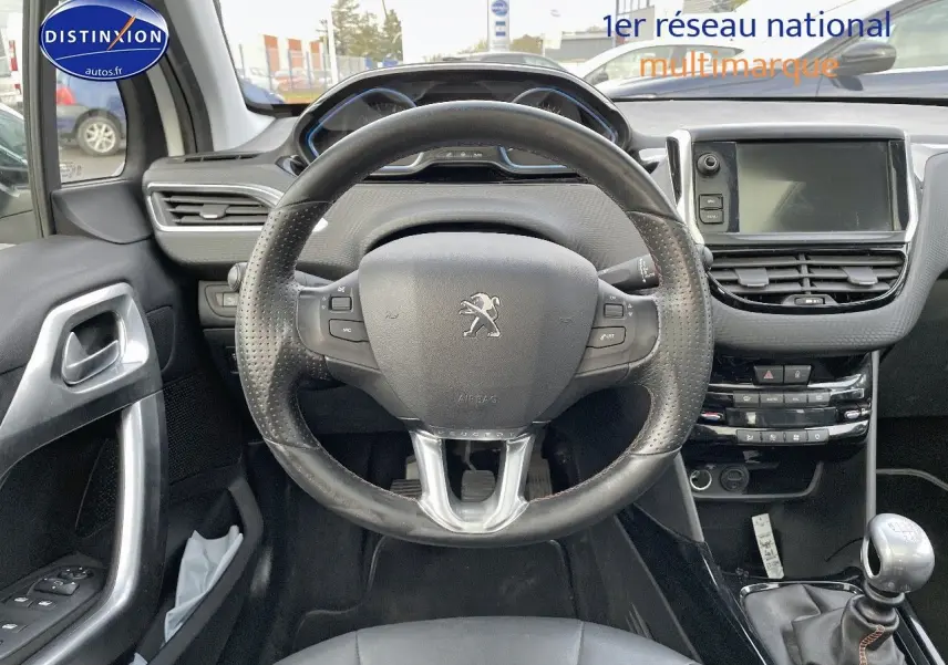 Vue intérieure centrée sur le volant cuir noir et la console centrale d'une Peugeot 2008 blanche de 2016 avec boîte manuelle.
