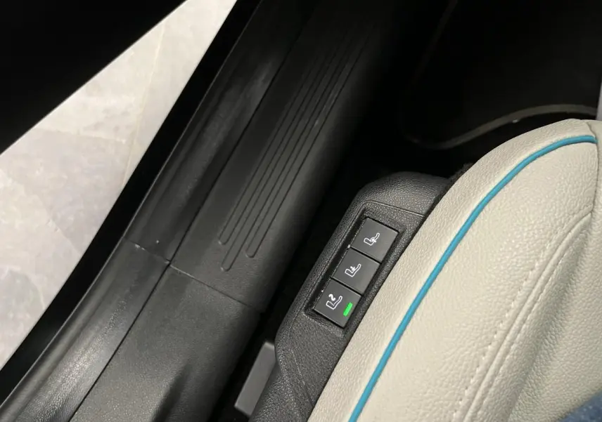 Gros plan sur les commandes de réglage électrique du siège conducteur ivoire soft touch de la FIAT 600 hybride noire.