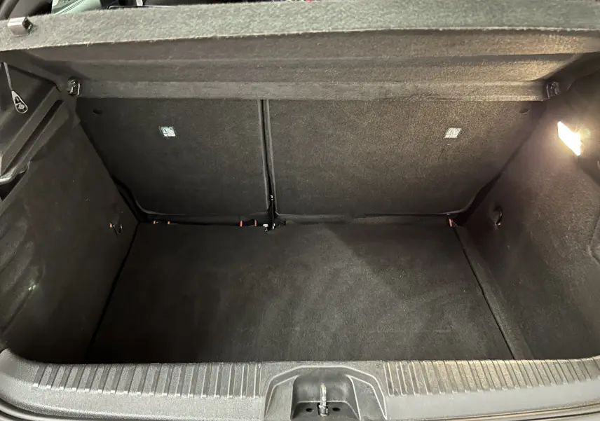 Coffre ouvert vu de l'arrière d'une Renault Clio V TCe 90 TECHNO rouge, intérieur noir avec éclairage à droite.