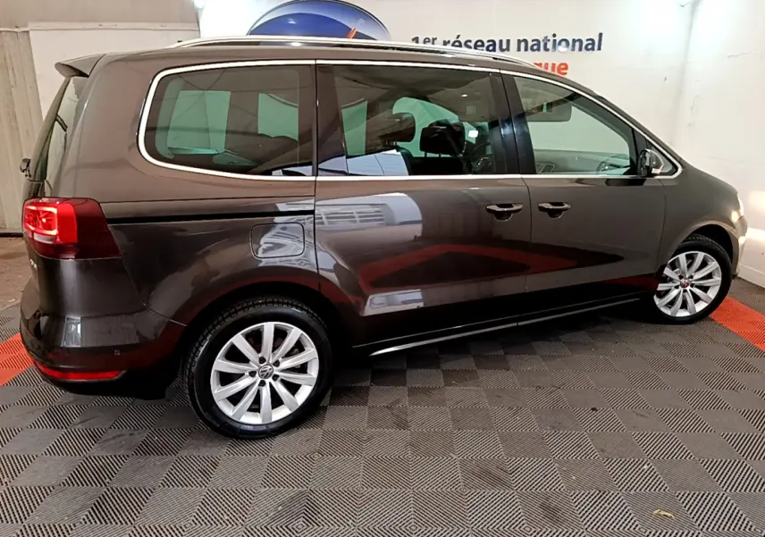 Vue de profil côté gauche d'un Volkswagen Sharan marron 2017 sur sol damier intérieur showroom.