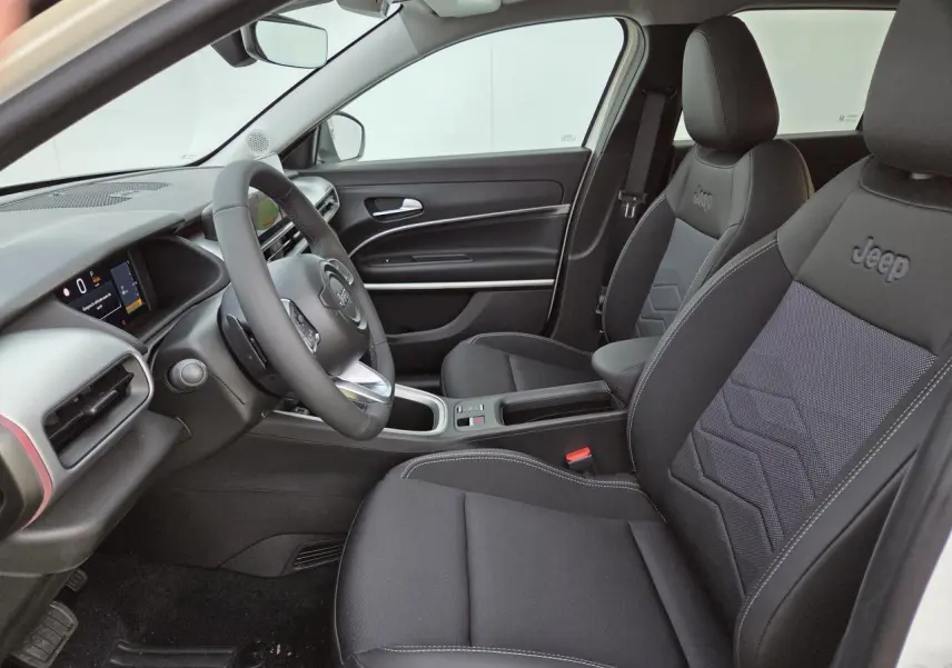 Vue intérieure côté conducteur du Jeep Avenger 2025, sièges noirs avec logo Jeep brodé et tableau de bord moderne.
