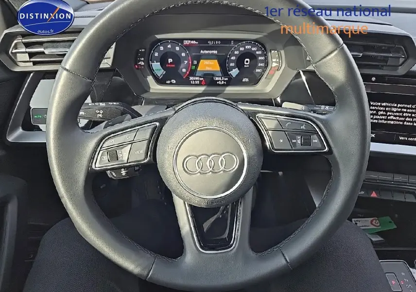 Vue intérieure centrée sur le volant cuir multifonction de l'Audi A3 Sportback gris Daytona avec tableau de bord digital.