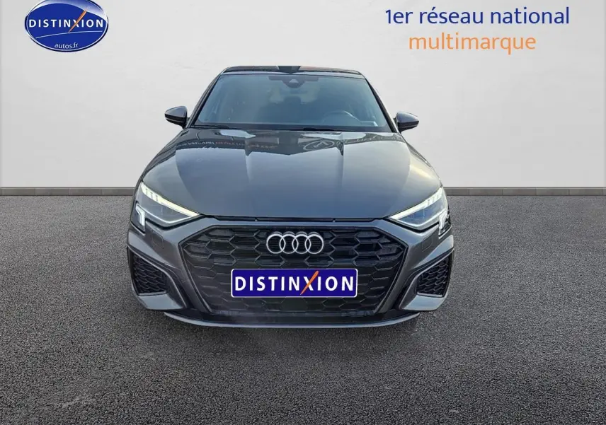 Vue frontale d'une Audi A3 Sportback gris Daytona avec calandre noire et phares LED allumés.