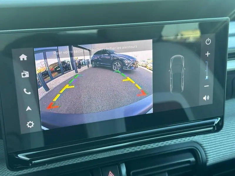 Vue caméra de recul montrant une Citroën C3 noire Perla Nera garée de biais côté droit devant un bâtiment vitré.