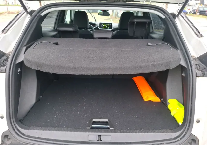 Coffre ouvert d’un Peugeot 2008 blanc nacré vue arrière, avec cache-bagages et gilets de sécurité visibles.