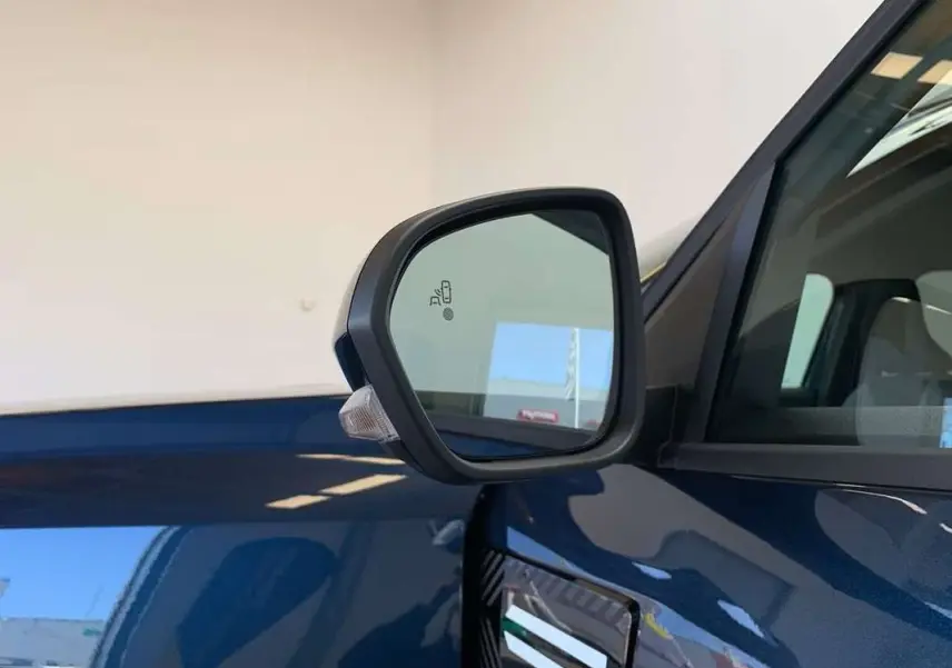Rétroviseur côté gauche du Dacia Bigster bleu indigo avec toit noir, montrant l'alerte d'angle mort intégrée.