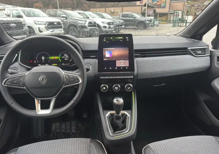 Vue intérieure avant de la Renault Clio V TCE 90 Techno Plus 2025, tableau de bord gris avec écran tactile vertical et boîte manuelle.
