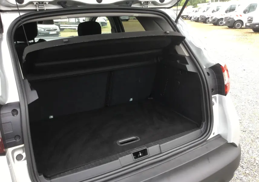 Coffre ouvert vu de l'arrière d'un Renault Captur gris clair métal avec intérieur noir, montrant l'espace de chargement vide.