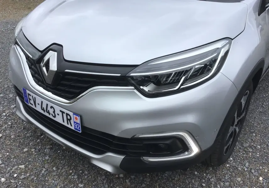 Vue 3/4 avant droit du Renault Captur gris clair métal avec calandre noire et signature lumineuse LED distinctive.