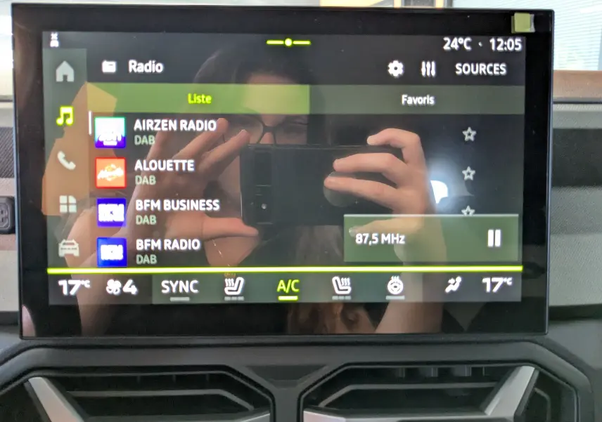 Écran tactile multimédia 10 pouces du Dacia Bigster Hybrid 155 Journey affichant les stations radio avec commandes climatisation visibles.