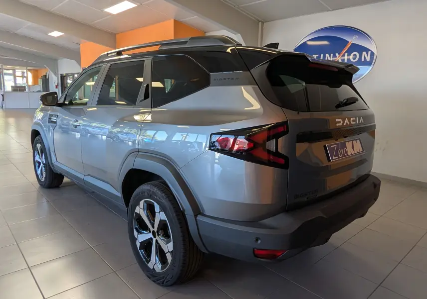 Vue 3/4 arrière droite du Dacia Bigster gris schiste avec toit bi-ton noir et jantes alliage diamantées en showroom.