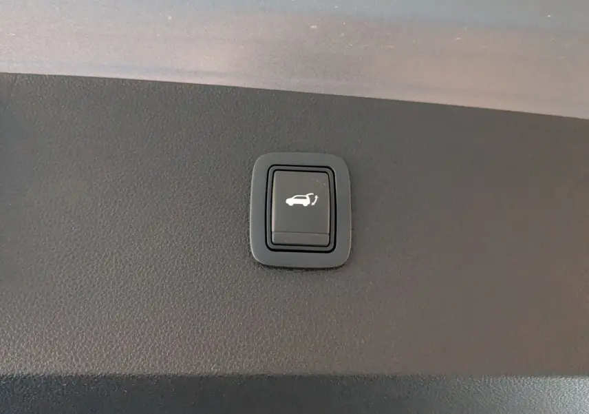 Bouton noir d'ouverture électrique du hayon sur la garniture intérieure du coffre du Dacia Bigster gris schiste.