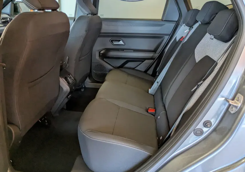 Vue intérieure côté droit des sièges arrière gris foncé du Dacia Bigster Hybrid 155 Journey avec portes ouvertes.