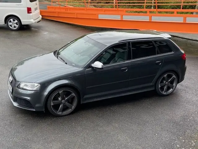 Audi RS3 Sportback gris Daytona vue de profil côté gauche, avec jantes noires et rétroviseurs argentés.