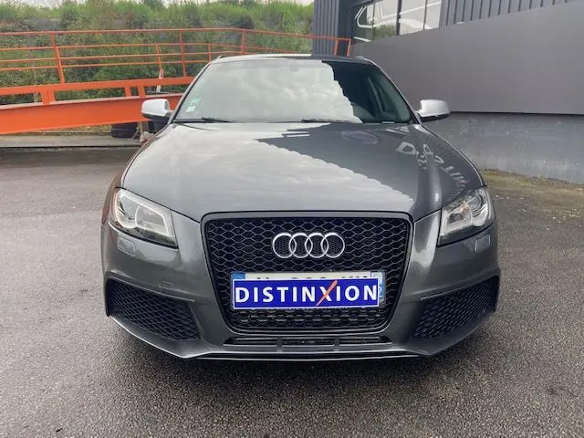 Vue frontale d'une Audi RS3 Sportback gris Daytona avec calandre noire et phares LED allumés.
