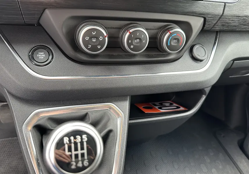 Gros plan sur la console centrale du Renault Trafic Combi gris comète, avec commandes climatisation et levier de vitesses manuel.