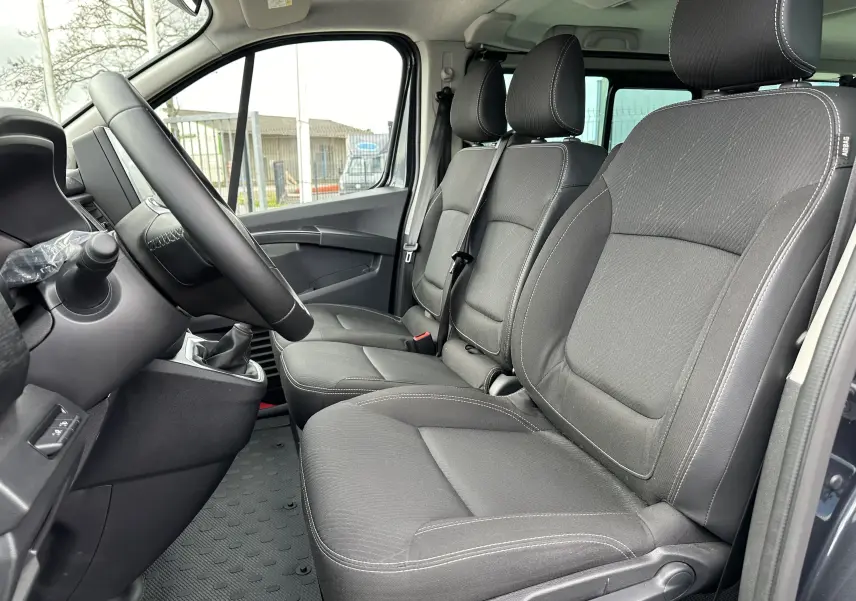 Vue intérieure côté conducteur du Renault Trafic Combi 2023, sièges tissu noir avec coutures blanches visibles.