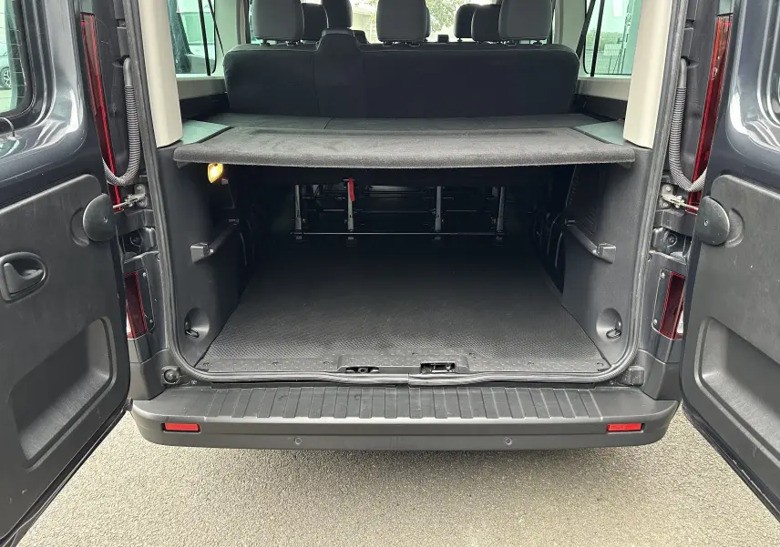 Vue arrière du Renault Trafic Combi gris comète 2023 avec portes ouvertes et espace de chargement visible.