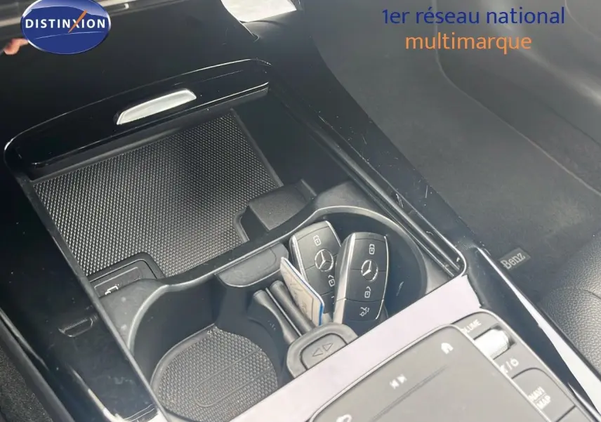Gros plan sur la console centrale noire brillante d'une Mercedes CLA Shooting Brake argent, avec clés et porte-gobelets visibles.