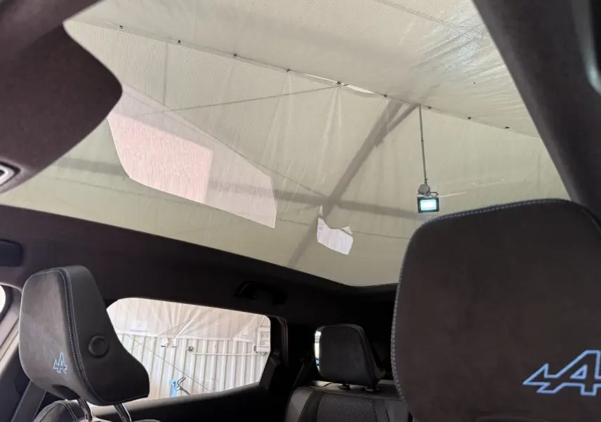 Vue intérieure du toit panoramique et sièges avant noirs avec logo Alpine bleu sur un Renault Espace gris foncé.