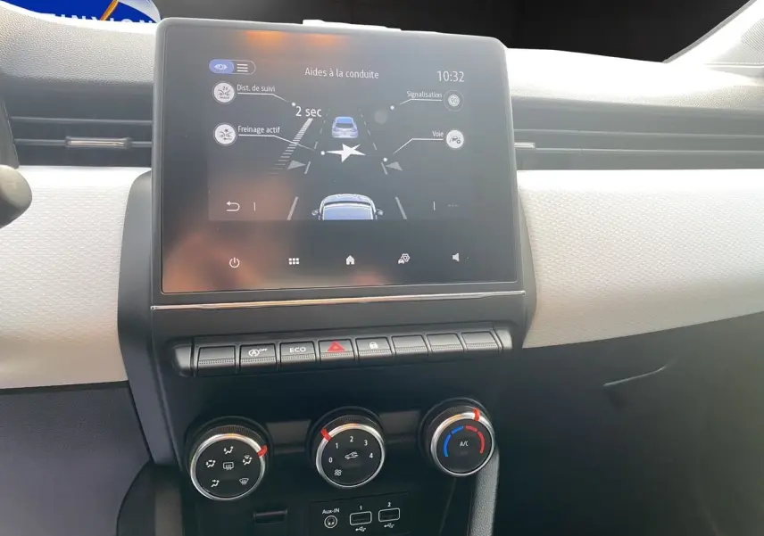 Vue rapprochée du tableau de bord beige de la Renault Clio V avec écran tactile 7 pouces et commandes de climatisation manuelle.