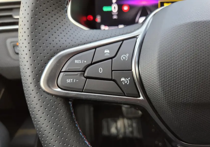 Gros plan sur les commandes du volant perforé noir avec surpiqûres bleues de la Renault Clio V hybride Gris Rafale.