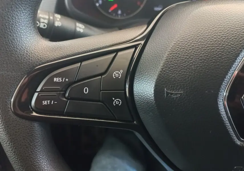 Gros plan sur les commandes du régulateur de vitesse sur le volant noir du Renault Trafic Fourgon blanc.