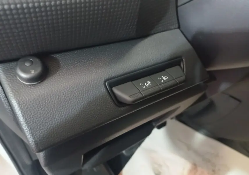 Gros plan sur les commandes de réglage manuel des phares à l'intérieur du Renault Trafic Fourgon blanc, côté conducteur.