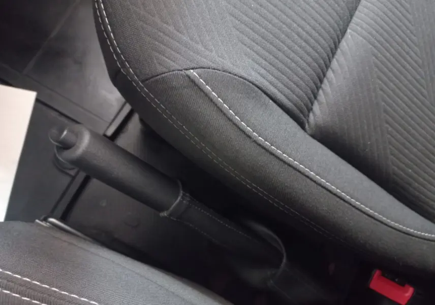 Vue rapprochée de la poignée de frein à main entre les sièges avant noirs du Renault Trafic Fourgon blanc.