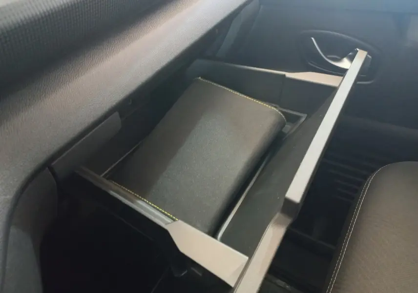 Tiroir de rangement ouvert côté passager dans l'habitacle du Renault Trafic Fourgon blanc, avec un carnet à l'intérieur.