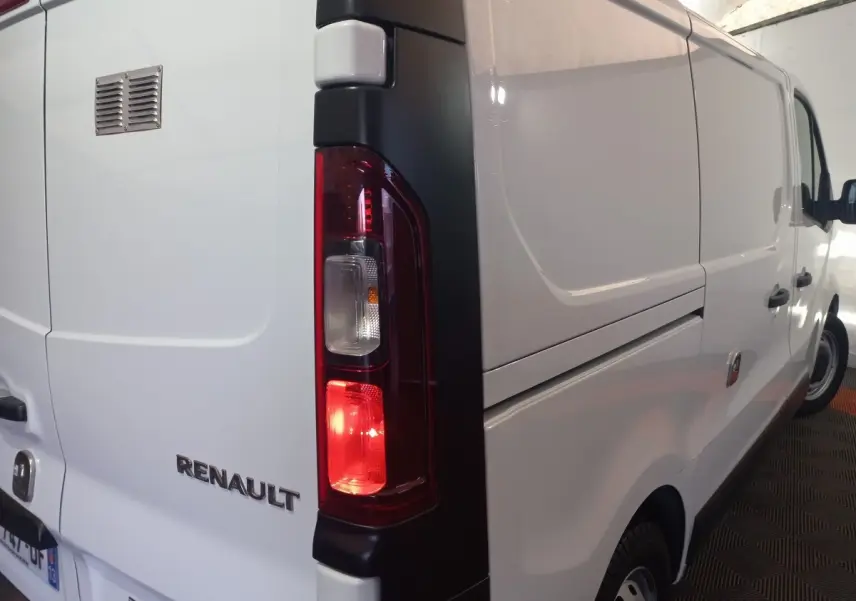Vue arrière côté gauche du fourgon blanc Renault Trafic FG GCF L1H1 3T avec feu arrière allumé et logo visible.