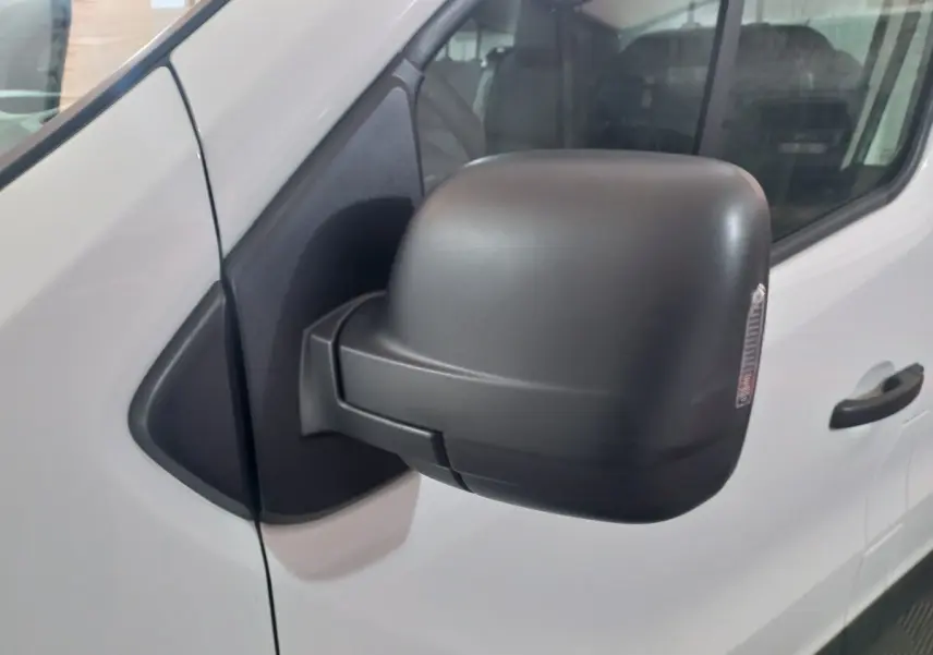 Gros plan sur le rétroviseur noir rabattable électriquement côté gauche du Renault Trafic Fourgon blanc.