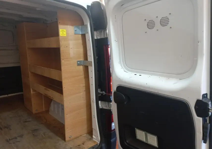 Vue arrière ouverte du Renault Trafic Fourgon blanc avec étagères en bois intégrées dans l'espace de chargement.