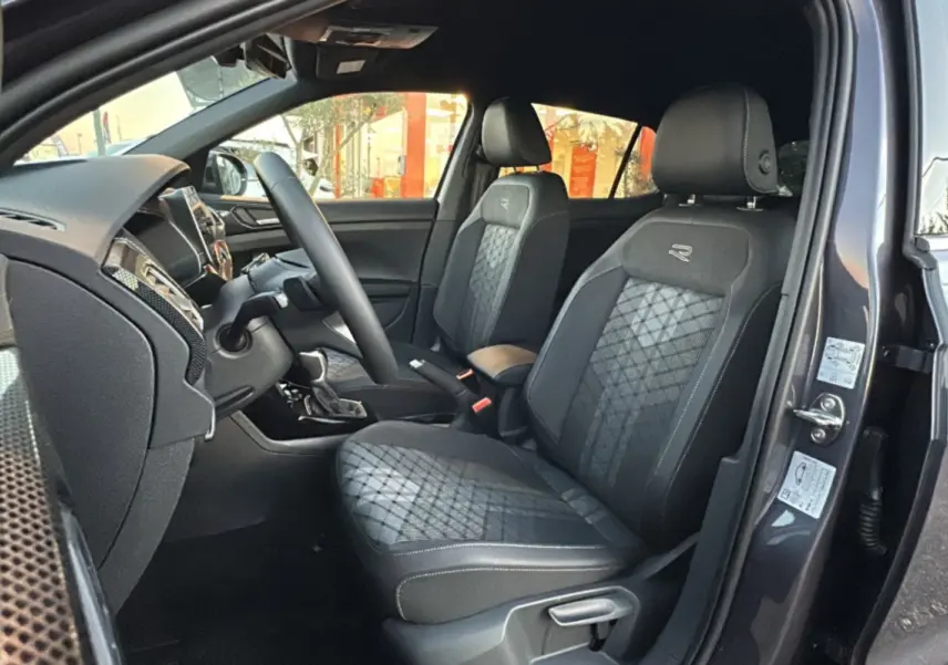 Intérieur avant du Volkswagen T-Cross gris cendré 2025, sièges tissu R-Line avec surpiqûres et volant multifonctions cuir.