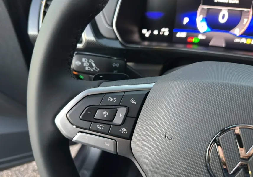 Gros plan sur le volant cuir multifonctions gris d’un Volkswagen T-Cross 2025 avec commandes de régulateur adaptatif.