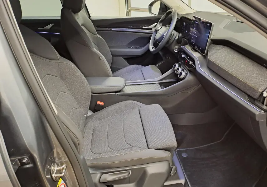 Vue intérieure côté conducteur du Skoda Kodiaq 2025 gris graphite, sièges tissu gris et tableau de bord moderne avec écran tactile.