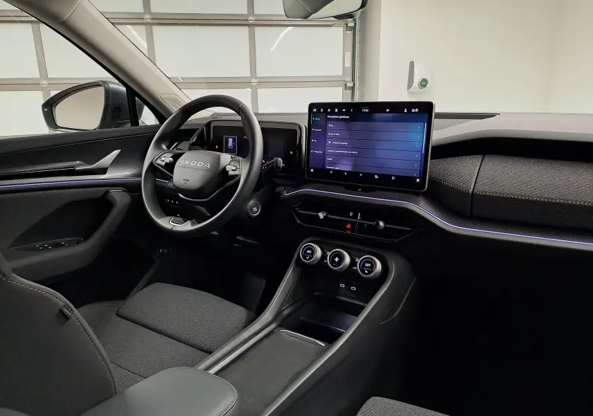 Vue intérieure côté conducteur du Skoda Kodiaq 2025, tableau de bord noir avec écran tactile central et éclairage d'ambiance violet.