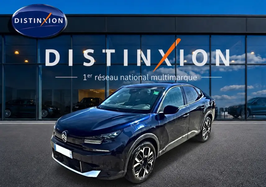 Citroën C4 X bleu en 3/4 avant droit, avec jantes alu et calandre distinctive, devant une vitrine Distinxion.
