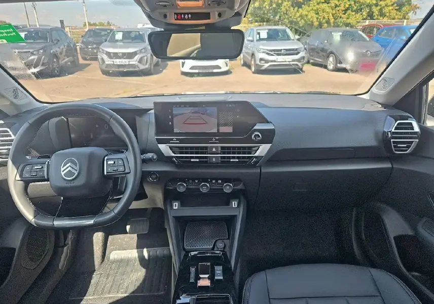 Vue intérieure avant du tableau de bord et volant cuir noir de la Citroën C4 X 1.2 hybride 2025 avec écran tactile et caméra de recul affichée.