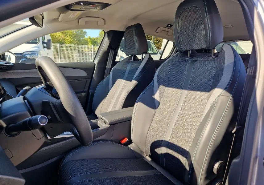 Vue intérieure côté conducteur de la Peugeot 308 1.2 Hybrid 145 Allure avec sièges tissu et cuir gris, volant multifonction.