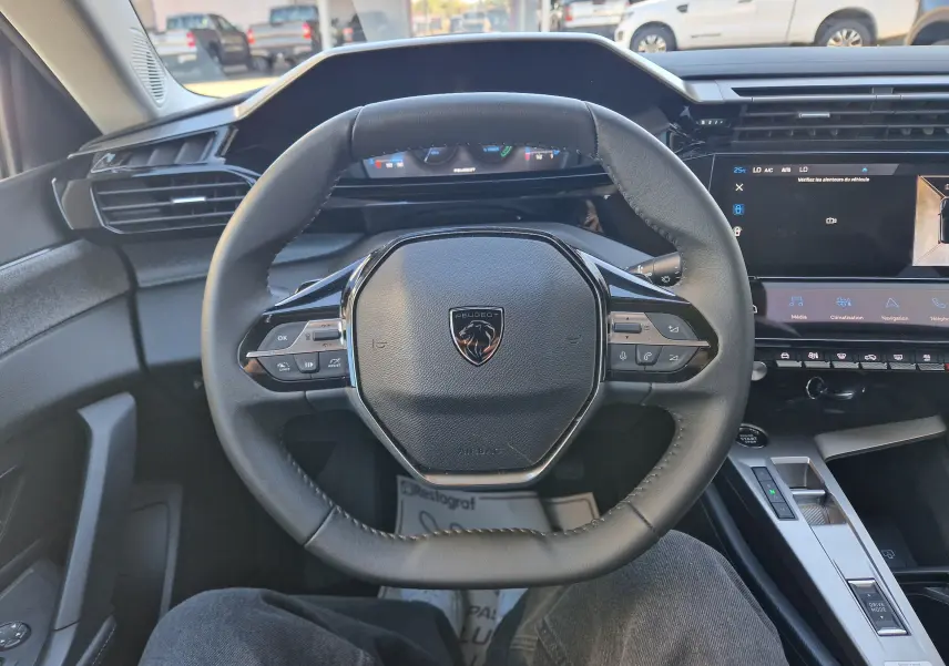 Vue intérieure centrée sur le volant cuir du Peugeot 308 gris Artense, avec tableau de bord digital et écran tactile visible.