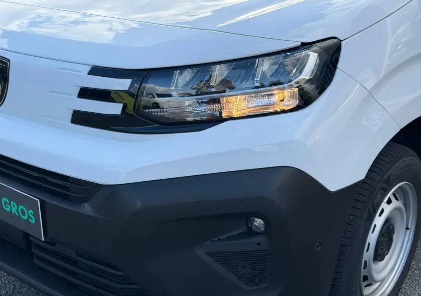 Gros plan sur l'avant droit du Peugeot Partner blanc Icy, avec phare allumé et pare-chocs noir mat.