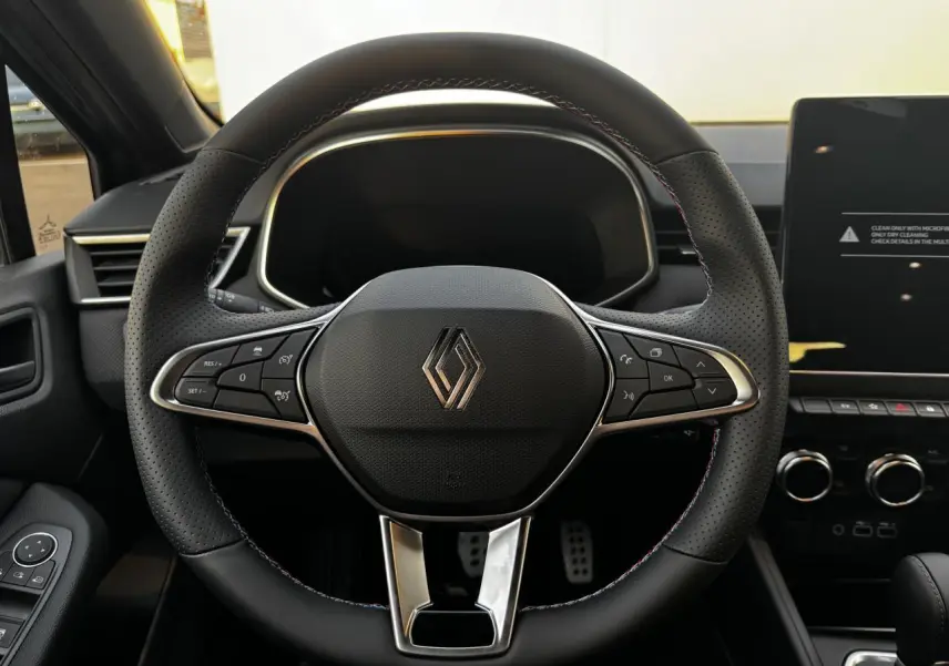 Volant perforé noir avec surpiqûres tricolores et logo Renault, tableau de bord et écran tactile à droite visibles