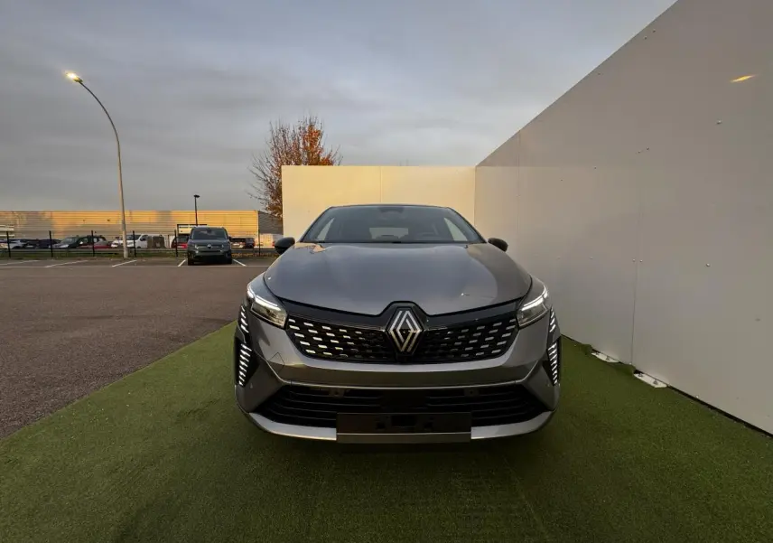 Vue de face d'une Renault Clio gris schiste métal avec calandre noire et feux LED verticaux allumés.