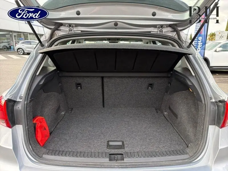 Coffre ouvert vu de l'arrière d'une SEAT Arona gris urbain métal, avec tapis gris et trousse de secours rouge.