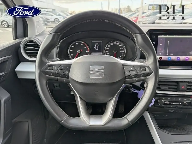 Vue intérieure centrée sur le volant cuir multifonction d'un SEAT Arona gris avec tableau de bord et écran tactile.