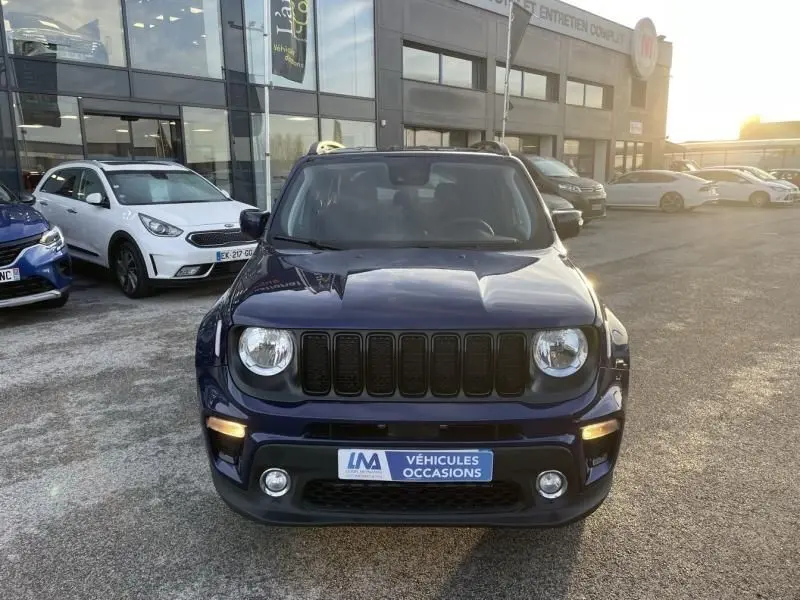 Vue frontale d'un Jeep Renegade bleu Jetset Metal 2021, avec calandre noire et feux ronds allumés, sur parking extérieur.